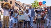 Lions-Maskottchen Leo, Lions-Präsidentin Dr. Lisa Huemke und Bürgermeister Thomas Beckmann überreichen den Gewinnerinnen und Gewinnern des Bücherlöwen Cups im Beisein ihrer Lehrerinnen Urkunde, Pokal und einen Scheck über 750 Euro der VR Bank in Holstein 